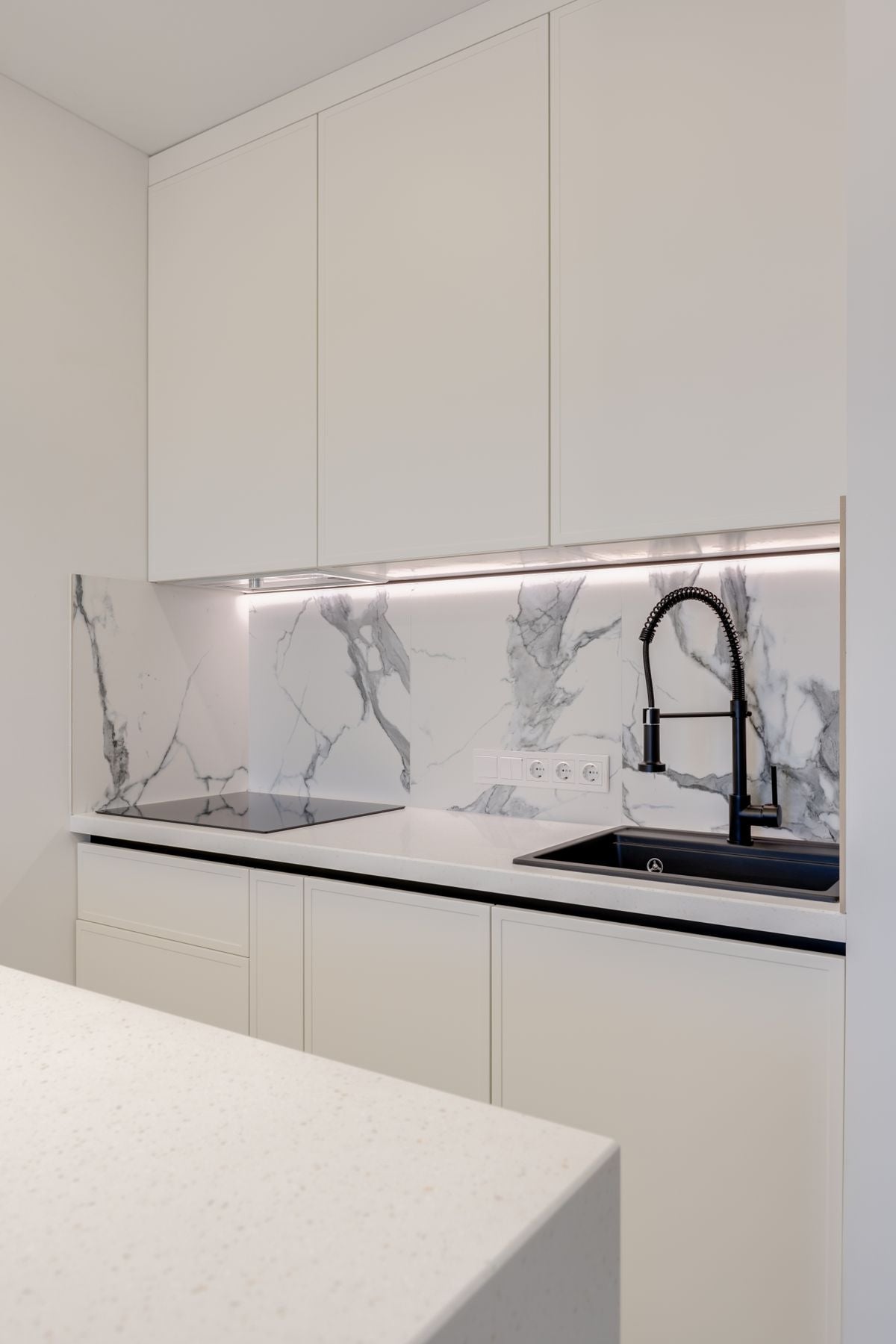 Elegant kitchen with white cabinets, marble backsplash and a black sink