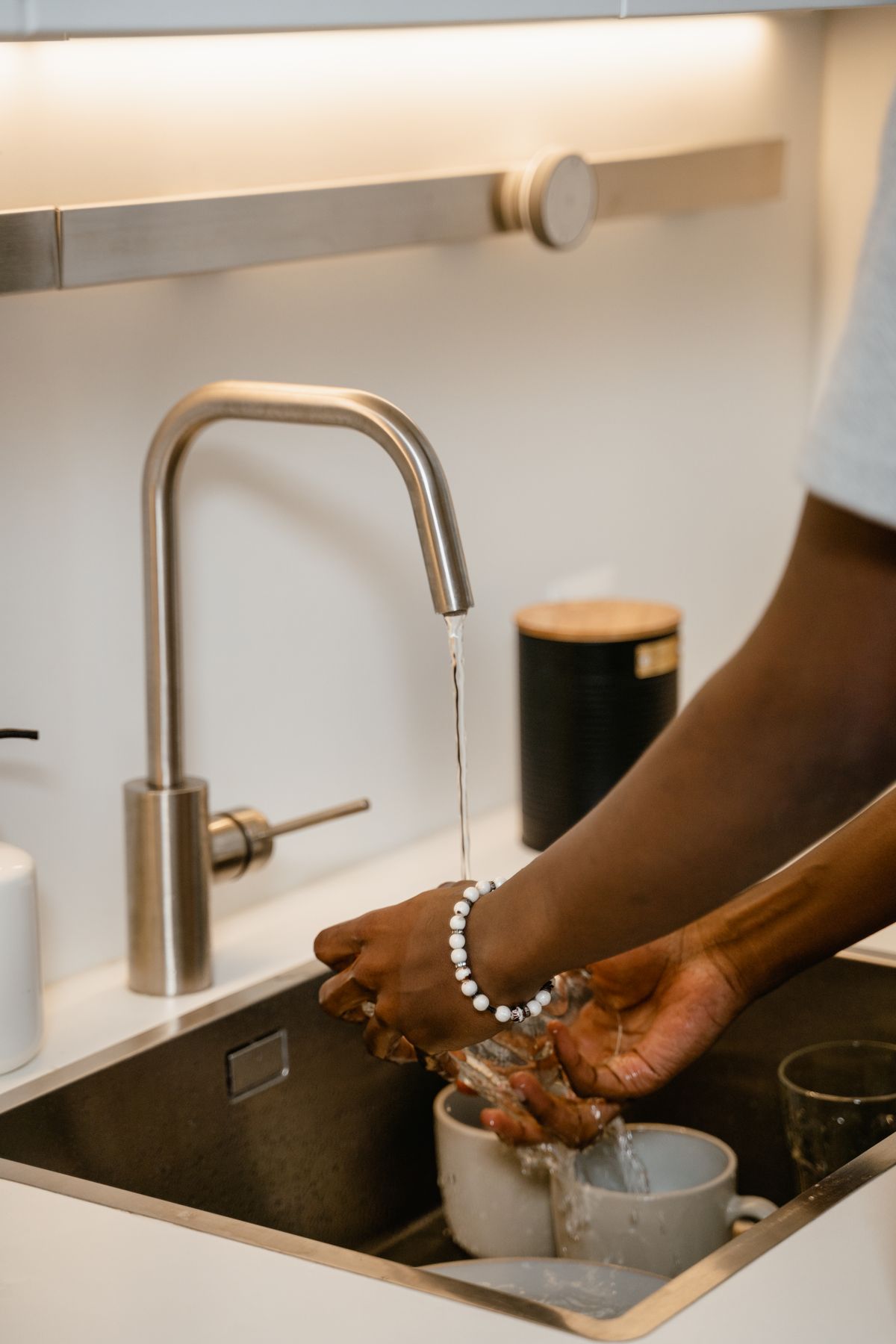 Hands washing dishes under a running kitchen tap